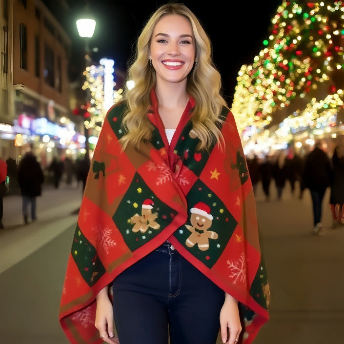 A woman standing on a festive Christmas street wearing a red and green holiday diamond-patterned wrap or poncho with gingerbread men and snowflake motifs. The background shows blurred holiday lights and trees.
