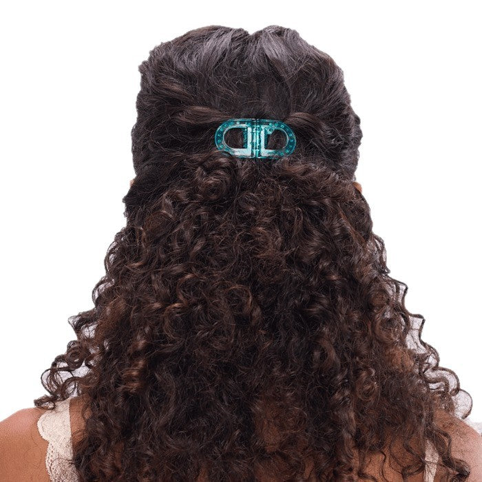 Back view of a person with long, dark brown curly hair secured with a translucent teal hair clip against a plain white background.