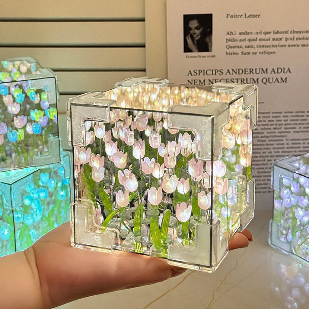 Transparent cube night light with floral design held by a hand, with blurred text in the background